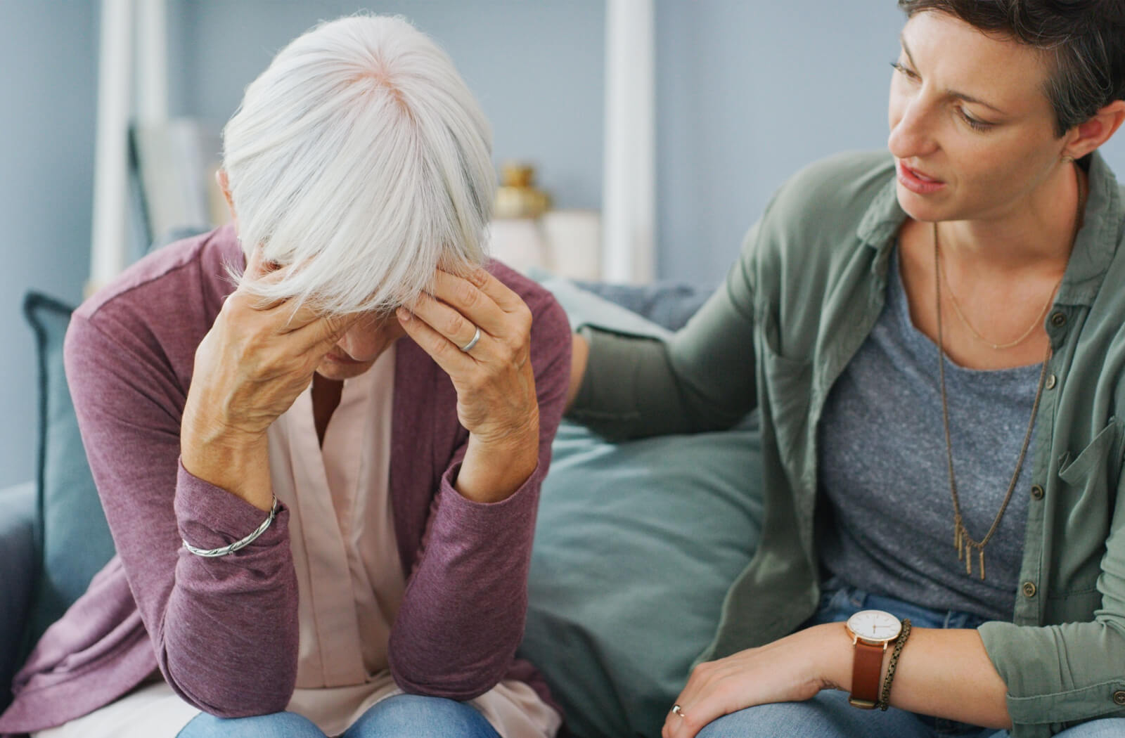 An adult comforting their parent as they rest their head in their hands in frustration due to dementia.