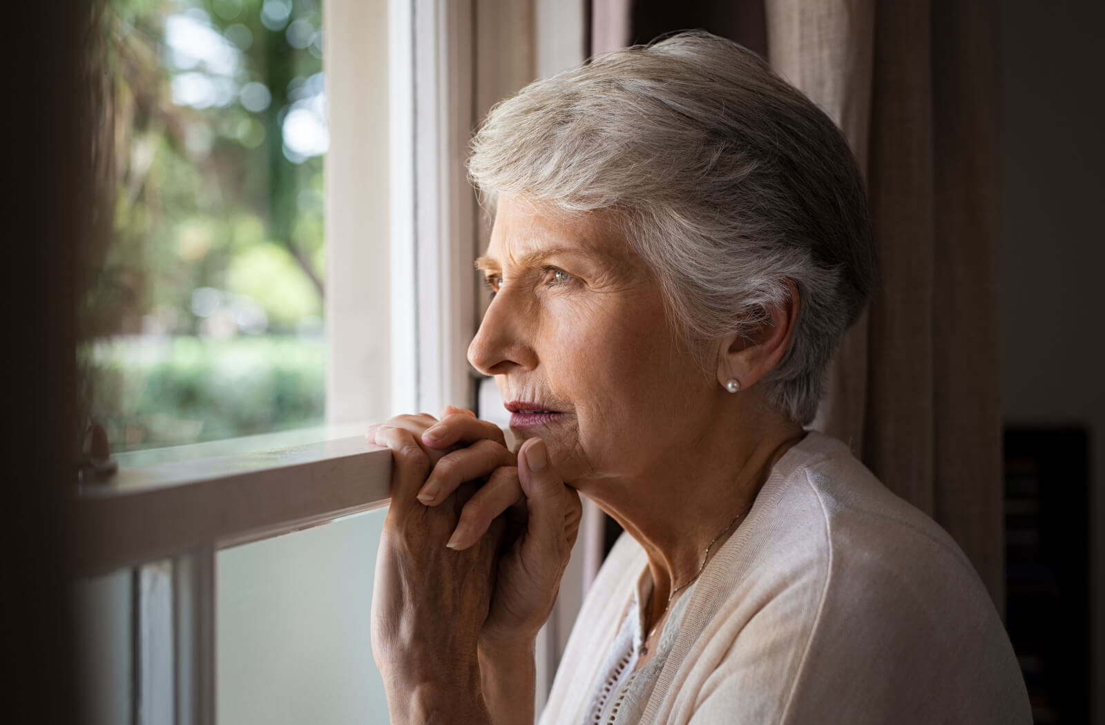 Sad and thoughtful looking senior woman stares out window.