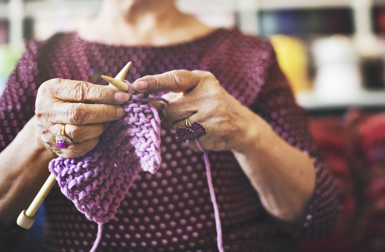 A close-up image of a senior crocheting with purple yarn.