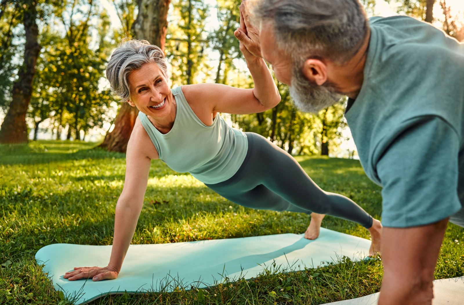 Two seniors performing a plank balance exercise outside, smiling and enjoying the activity outside