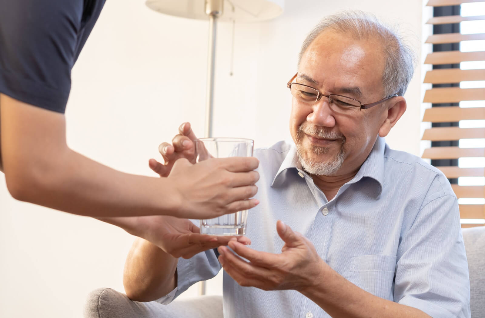 a caregiver hands a glass of thickened water to a senior man