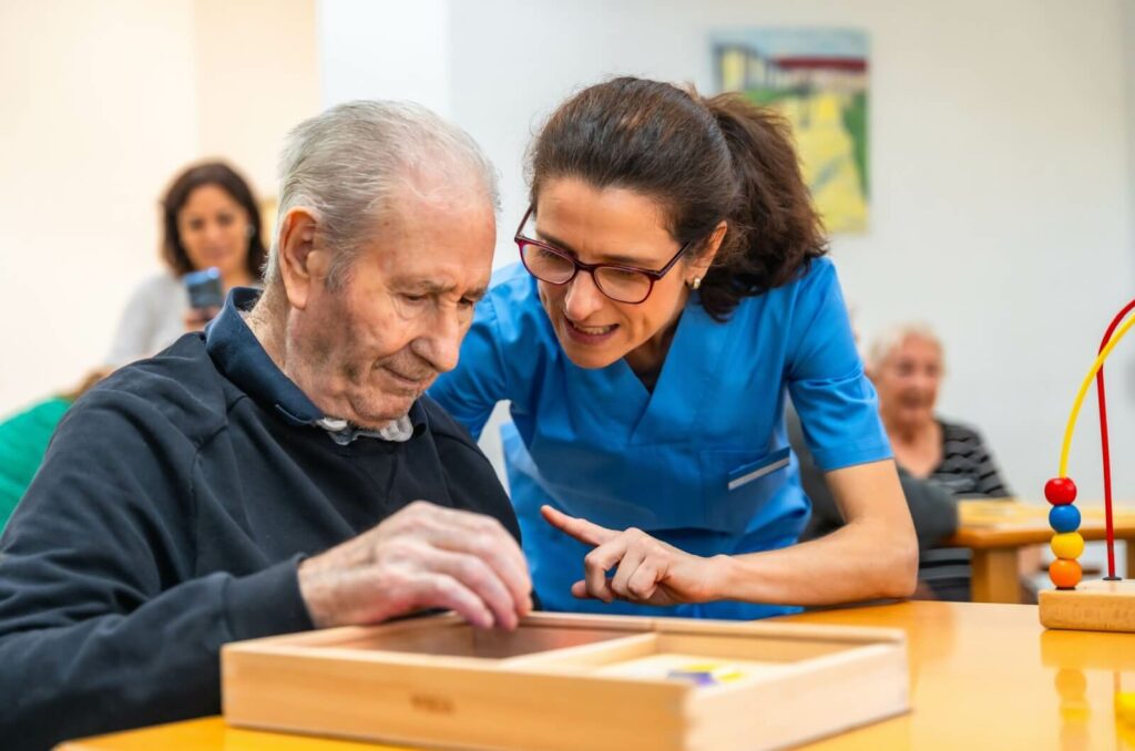 a carer helps a senior in memory care do a puzzle