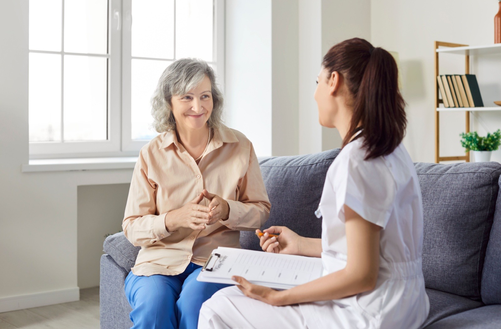 a senior and a carer sit on a couch completing a form